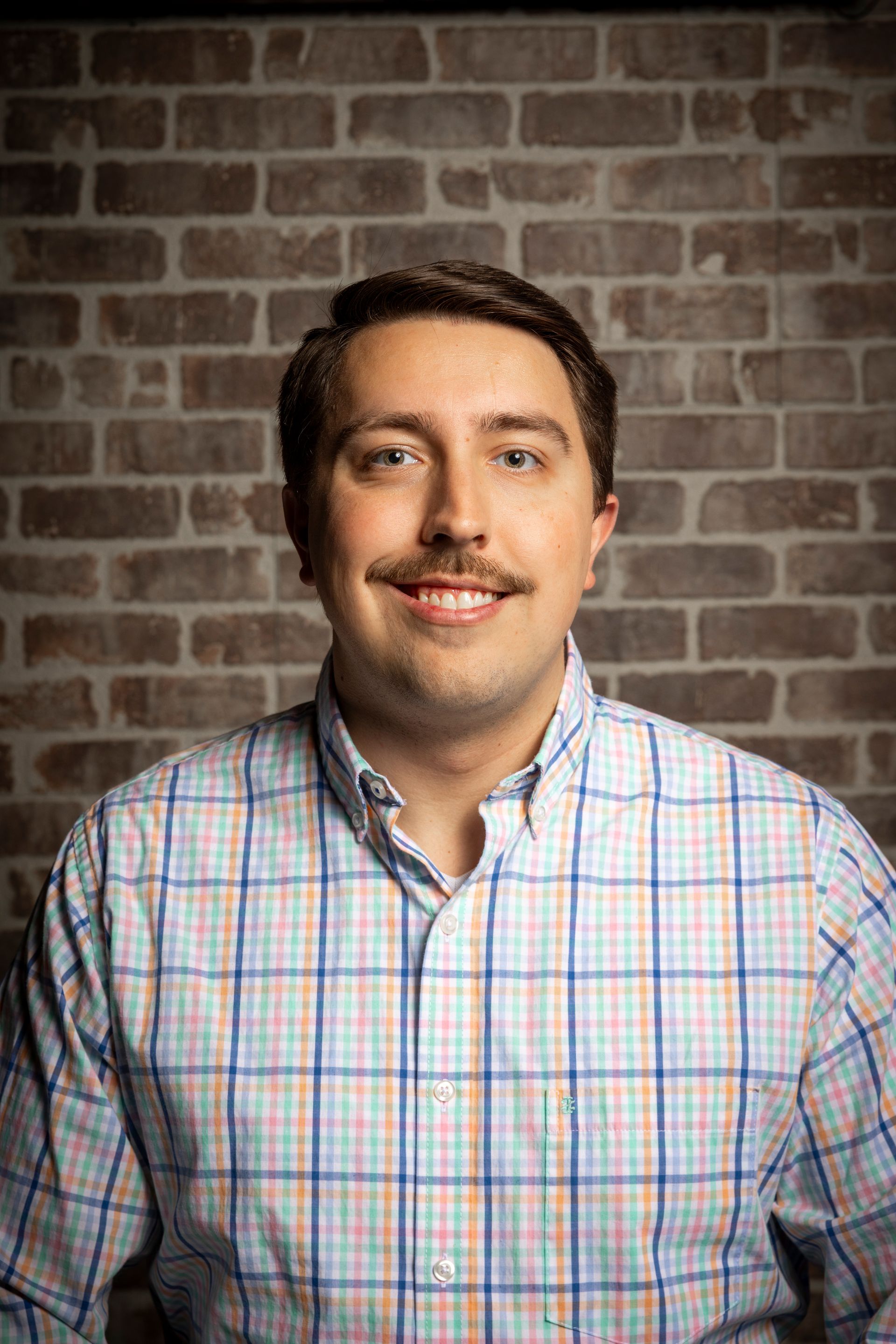 Smiling man in a plaid shirt standing before a brick wall background