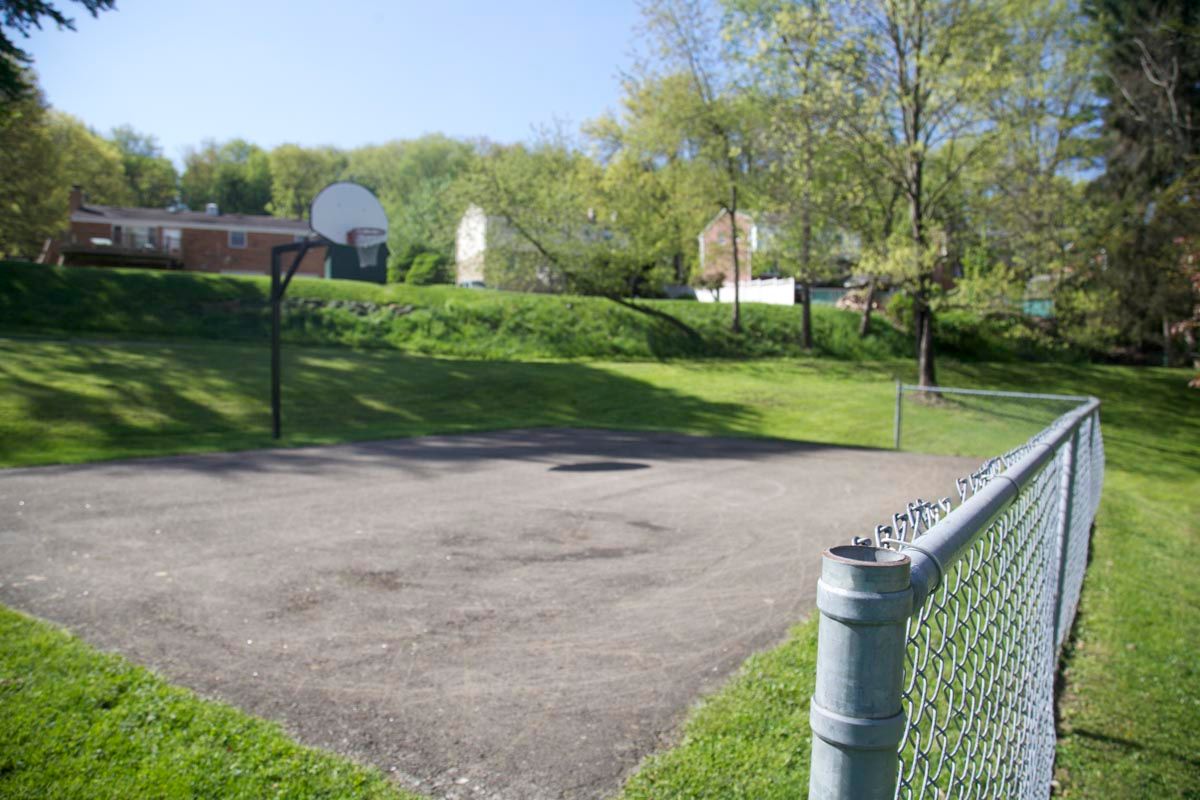 Empty asphalt court beside a chain-link fence and grassy hill under a blue sky
