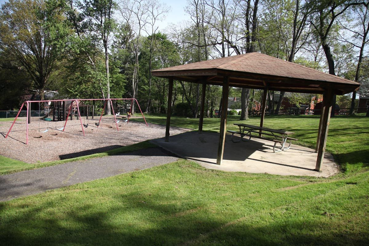 Park pavilion beside a playground with swings, surrounded by grass and trees