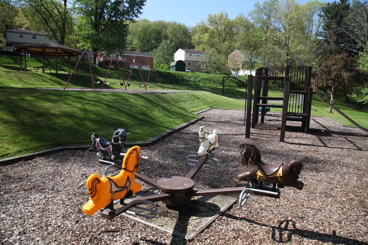 Playground with spring riders and a climbing structure on a sunny grassy hillside