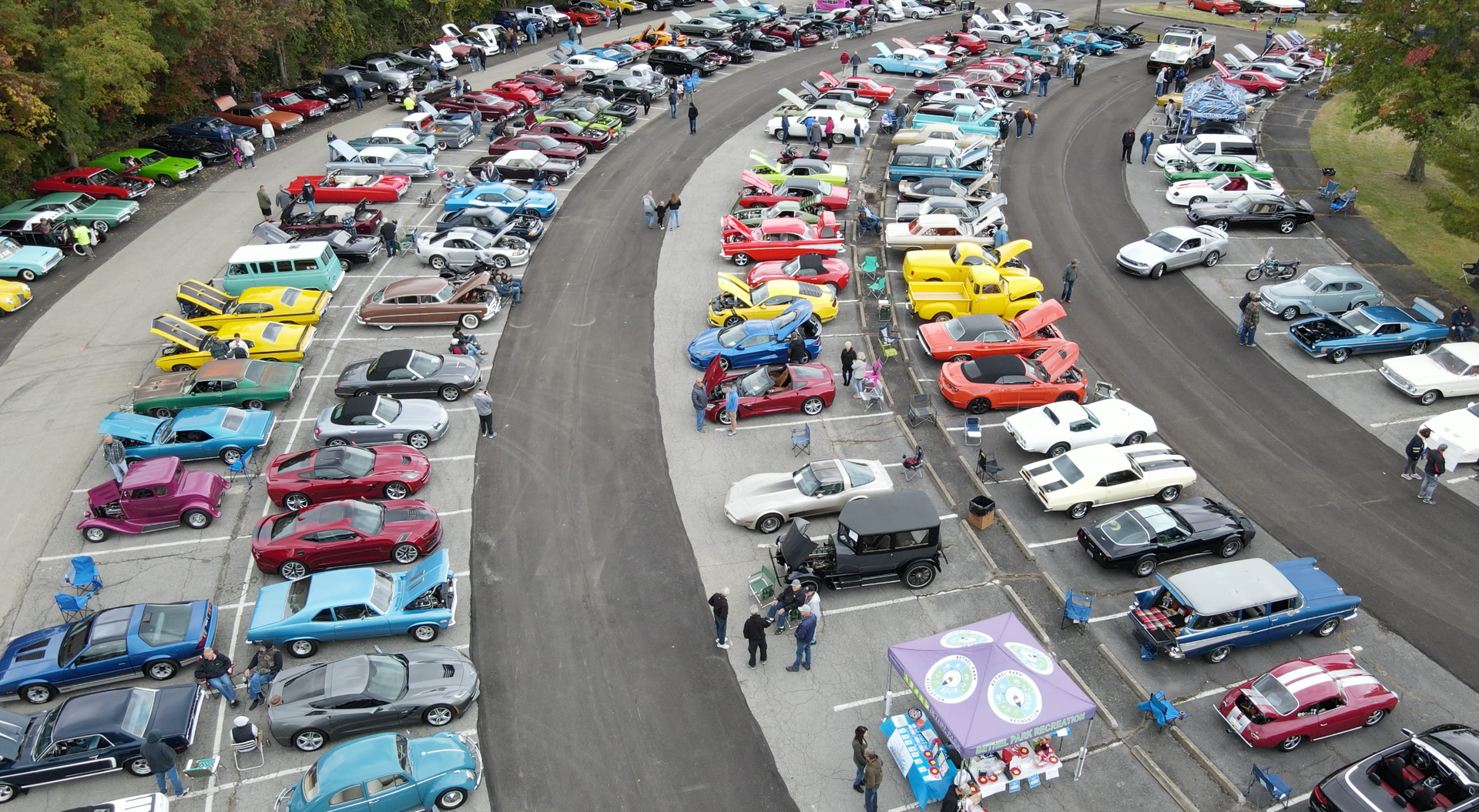 Aerial view of rows of colorful classic cars parked along a winding road at a car show.
