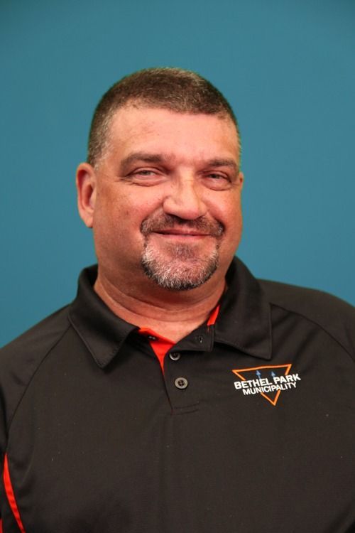 Man smiling in a black polo shirt against a blue background.