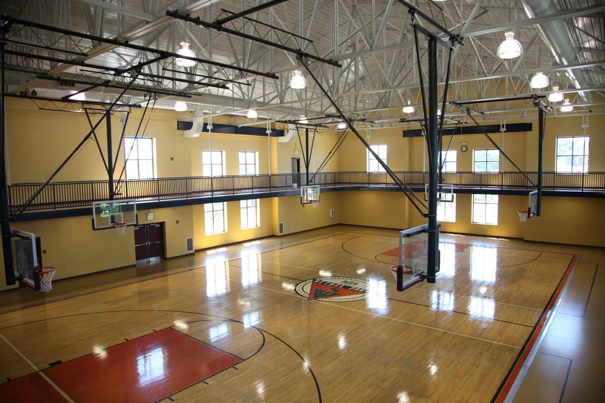 Indoor basketball gym with polished wood floor, hoops, and bright overhead lights
