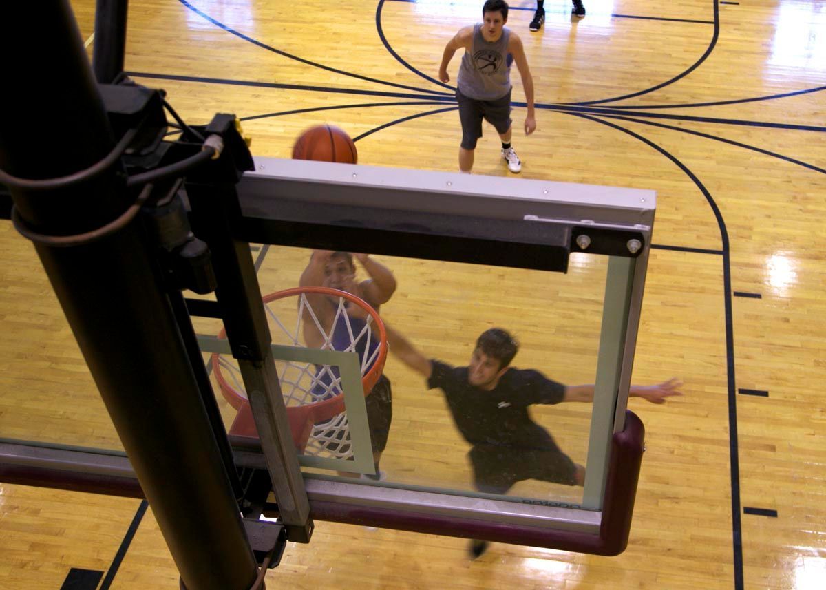 Basketball hoop from above, with a player jumping near the rim on a gym court.