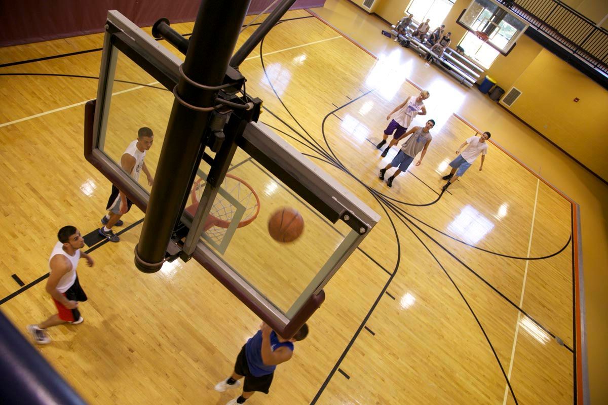 Basketball game in a gym, viewed from above near the hoop, with players on the court.