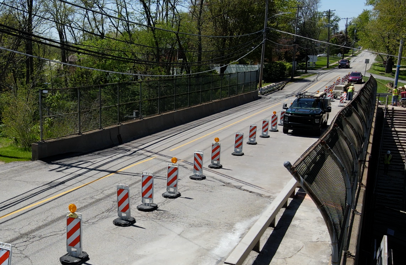 Coned-off road lane with a black SUV driving through a narrow construction area near a bridge.