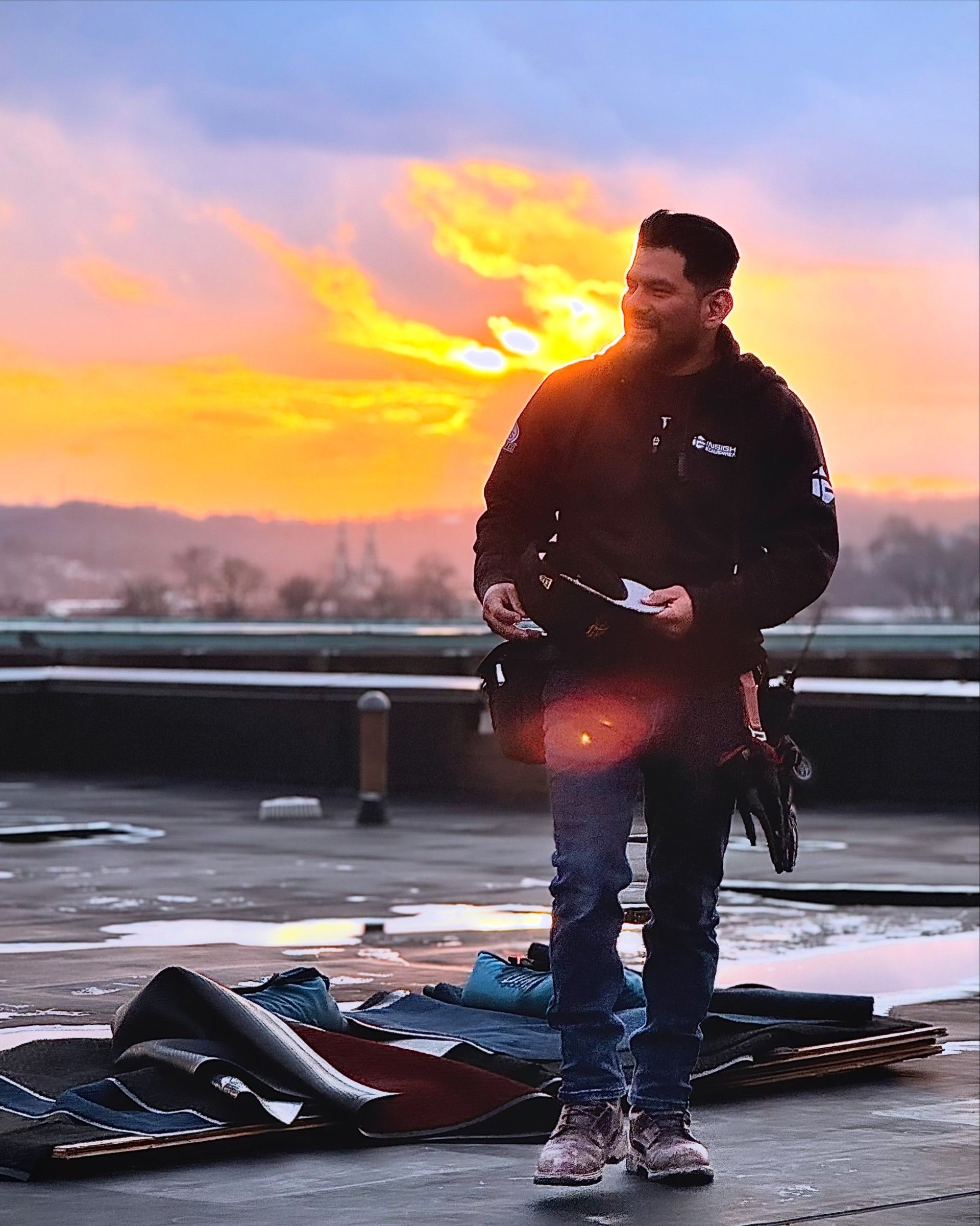 Person standing on a rooftop at sunset beside scattered equipment, with a vivid orange sky behind.
