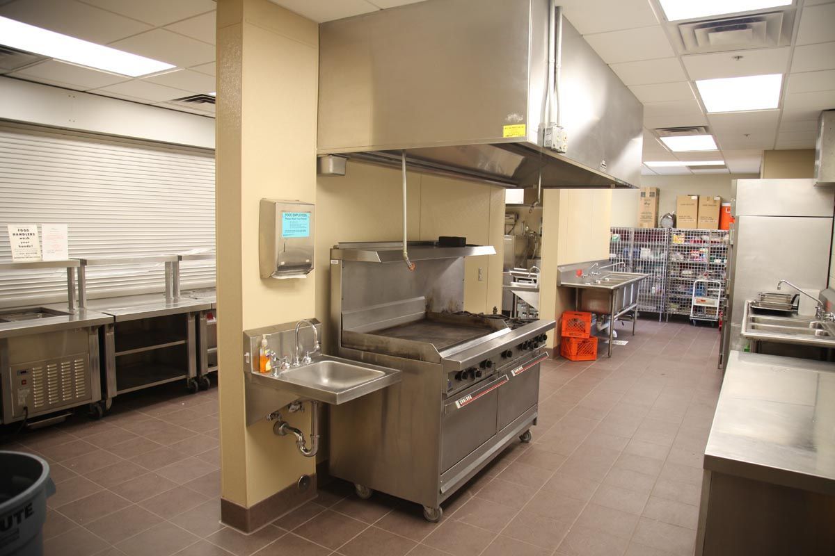 Commercial kitchen with stainless steel stoves, counters, and prep equipment in a tiled room