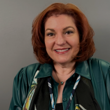 Smiling woman in a teal jacket and patterned scarf against a gray background
