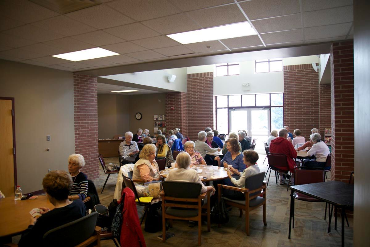 People seated at tables in a bright cafeteria, chatting over a meal.