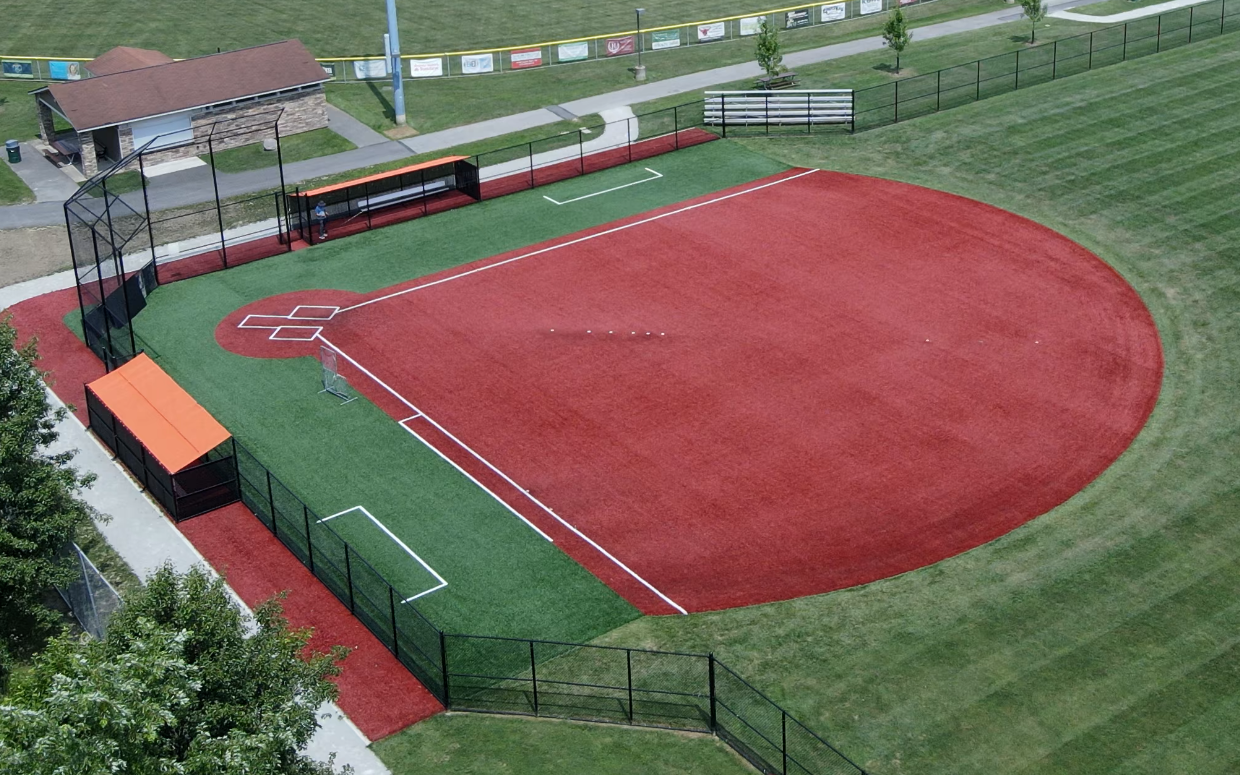 Aerial view of a baseball field with a red infield, green outfield, and surrounding fence and bleachers