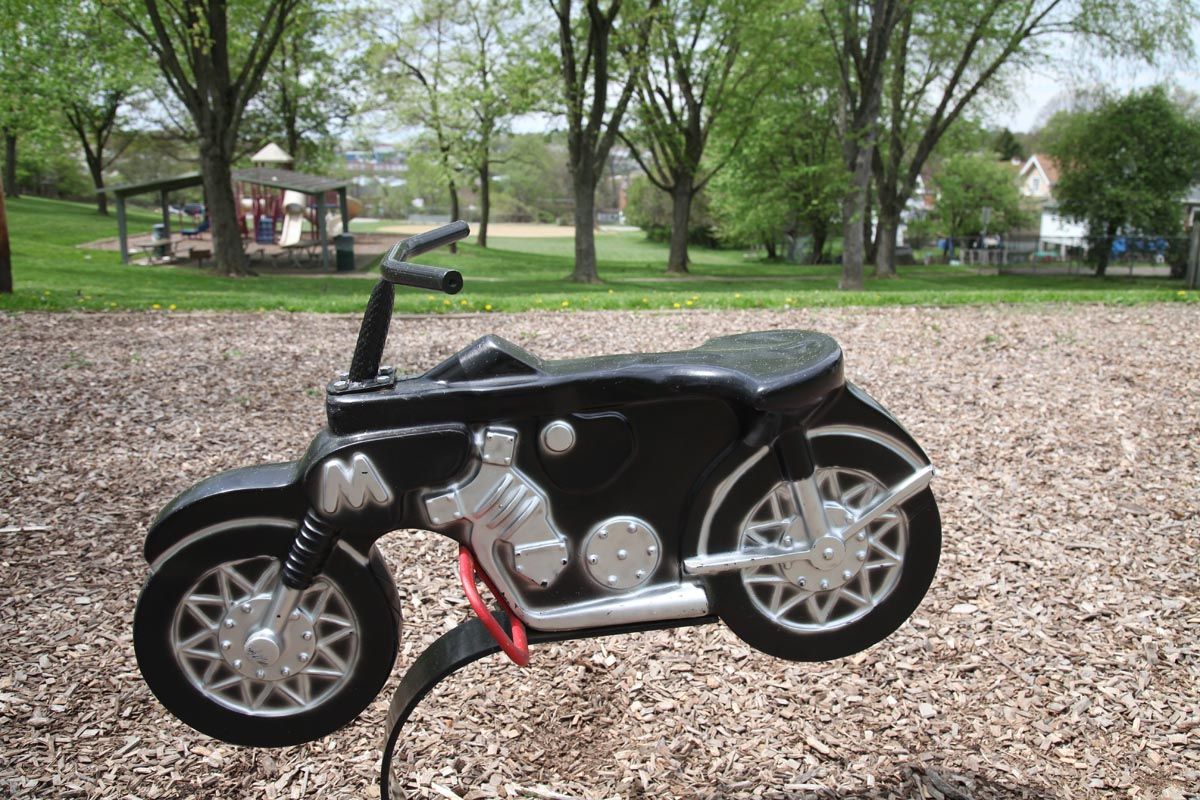 Black custom miniature motorcycle on gravel in a park with trees in the background