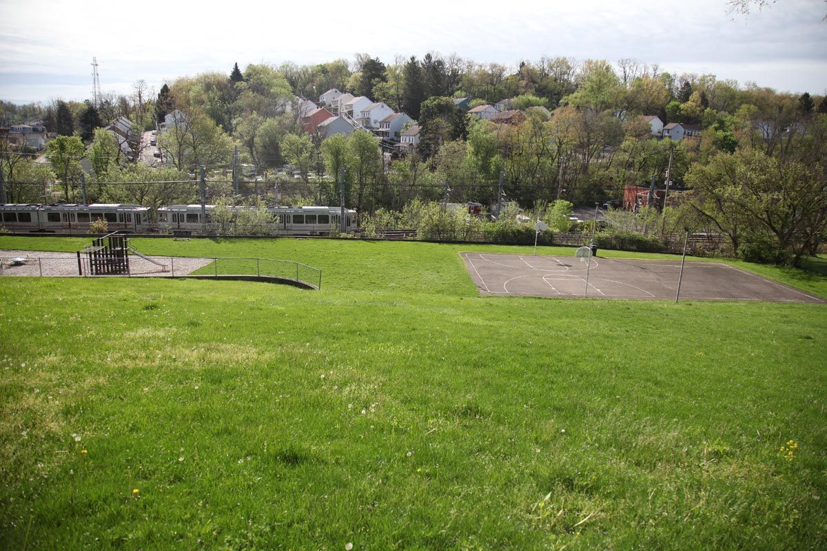 Grassy park with a hillside neighborhood and trees in the background, under a bright sky