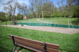 Park bench overlooking a fenced tennis court and grassy park under blue sky
