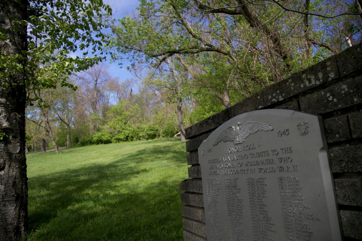 Stone memorial plaque beside a grassy hill and trees in a park