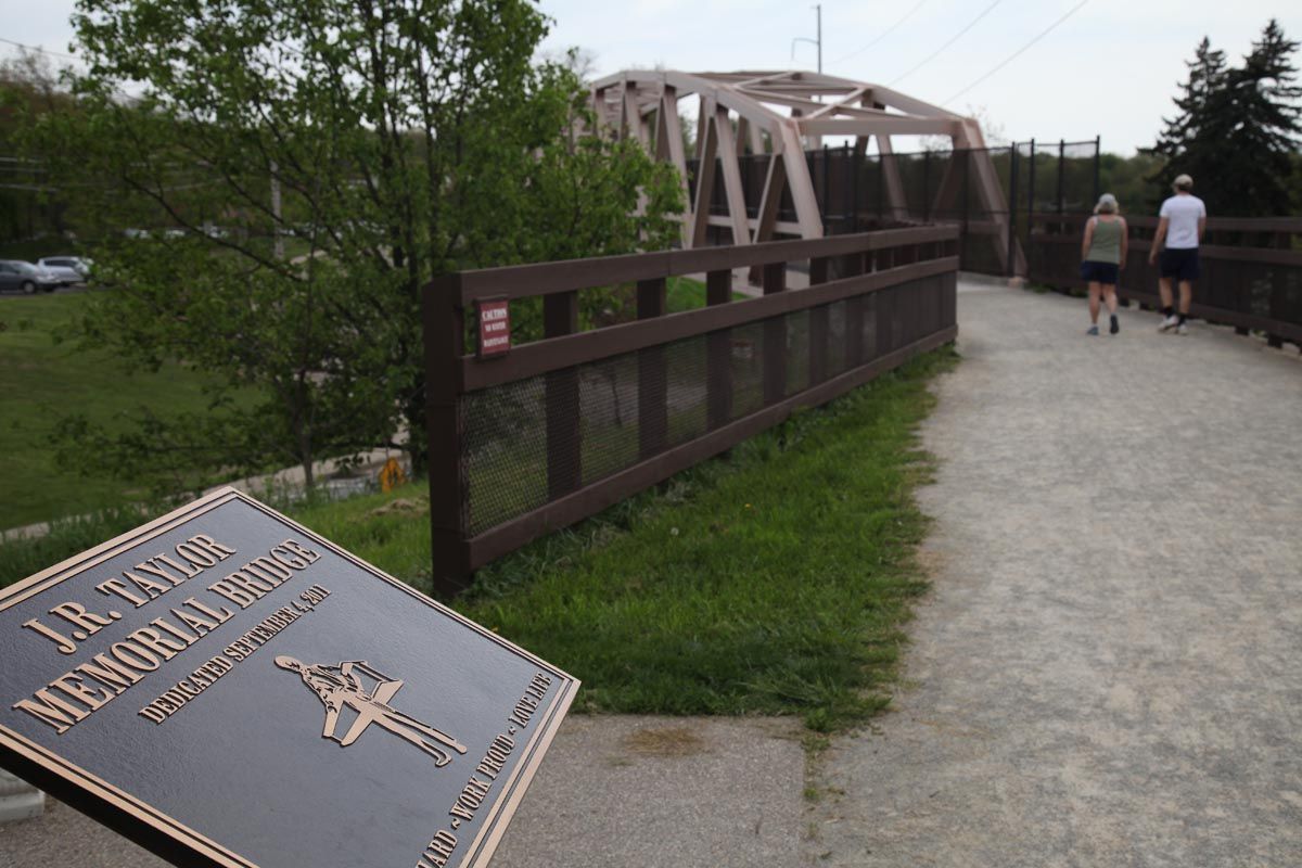 Curved walkway on a bridge with a memorial plaque in the foreground and two people walking ahead