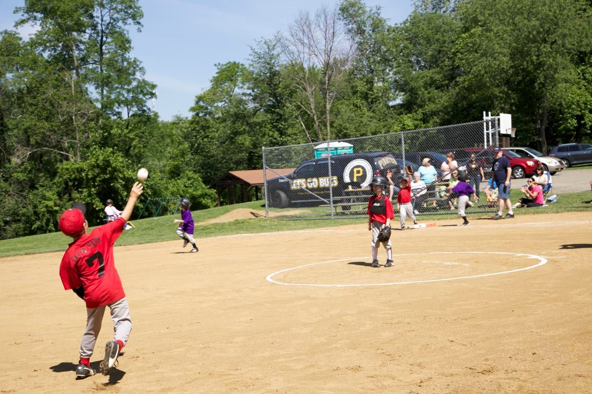 Youth softball game on a sunny field, with a red-clad player pitching toward the batter.