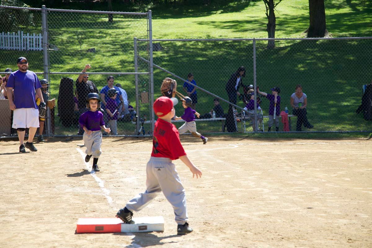 Child in red shirt running past a base on a baseball field during a game