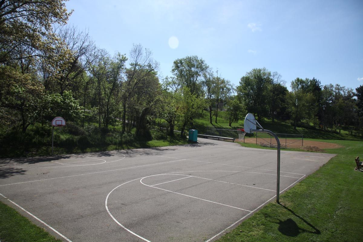 Empty outdoor basketball court surrounded by trees under a bright blue sky