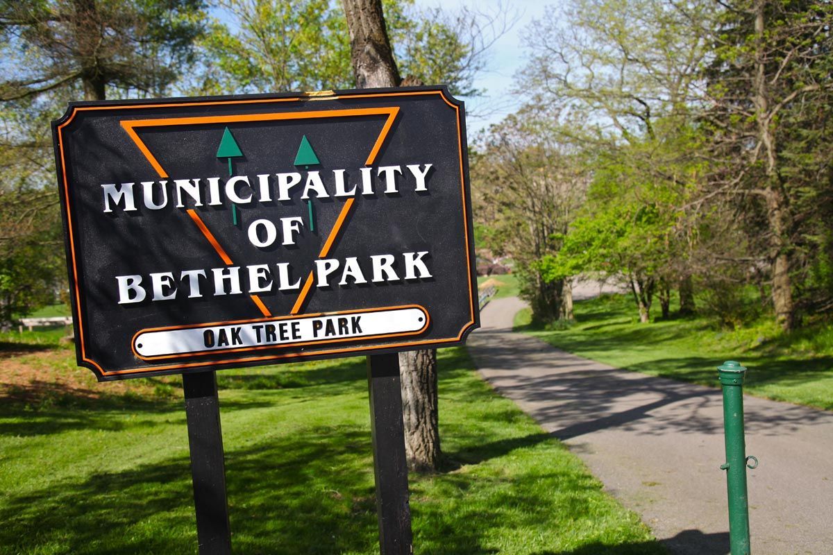 Bethel Park sign beside a tree-lined park path on a sunny day
