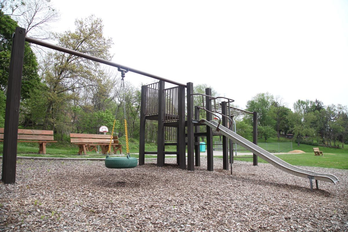 Playground with a slide, climbing structure, swings, and wood-chip ground in a park
