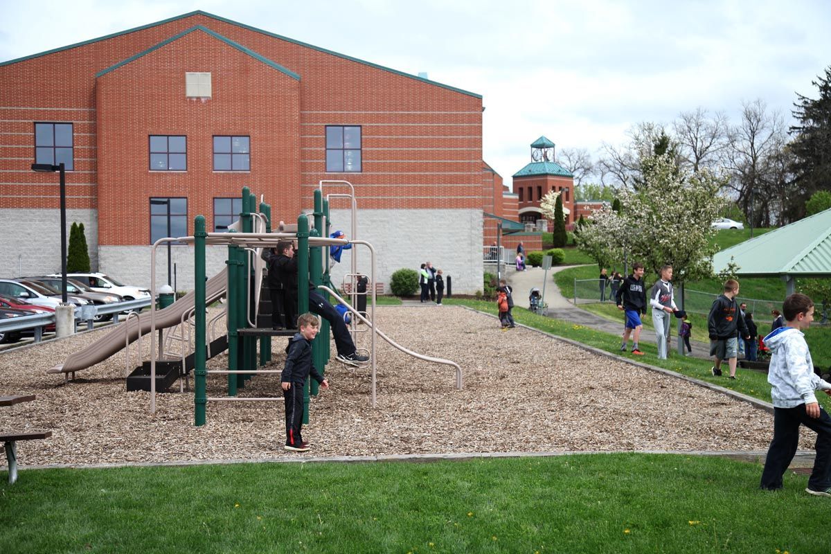 Children playing on a playground beside a red brick building on a sunny day.
