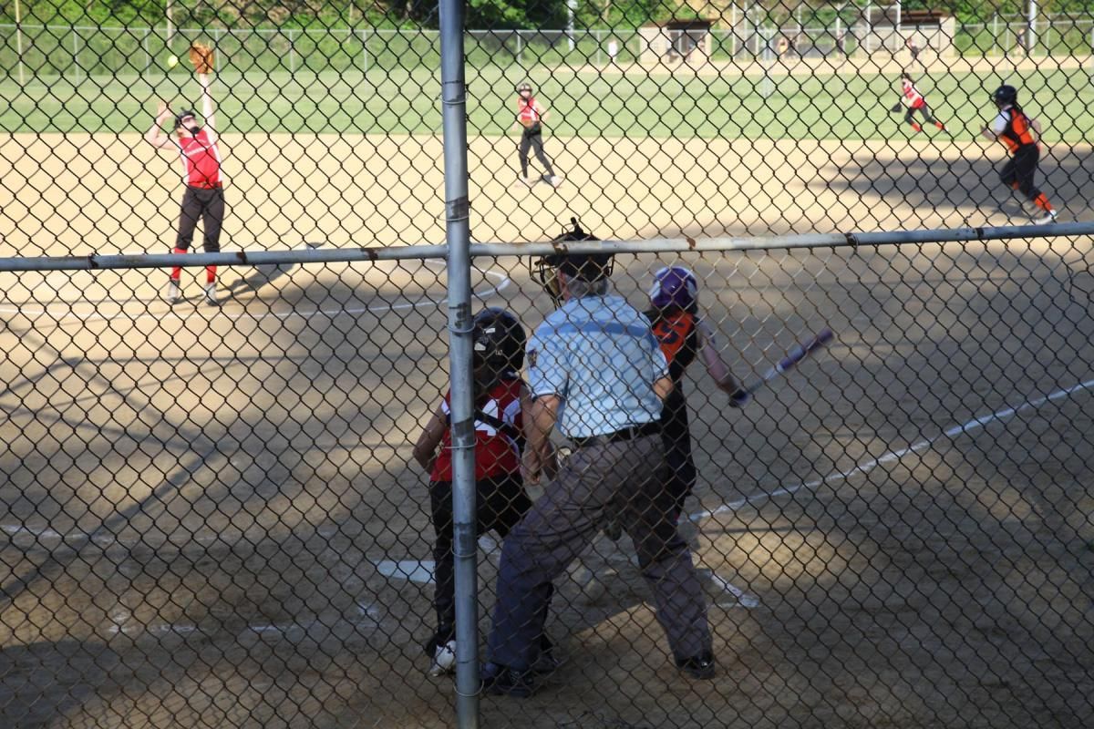 Youth softball game with batter, catcher, umpire, and fielders behind a chain-link fence