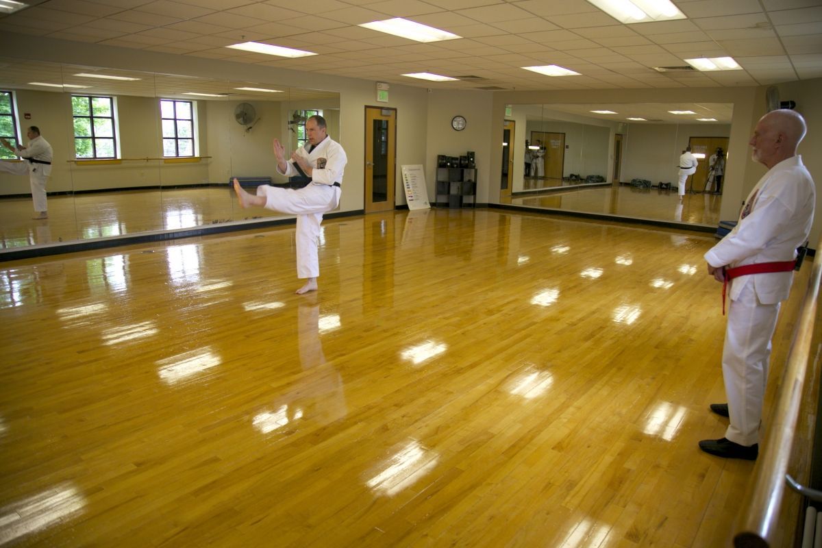 Martial arts class practicing kicks in a mirrored studio with polished wooden floors