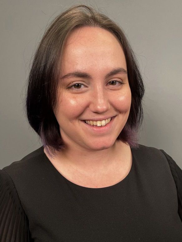 Smiling person with short brown hair wearing a black top against a gray background