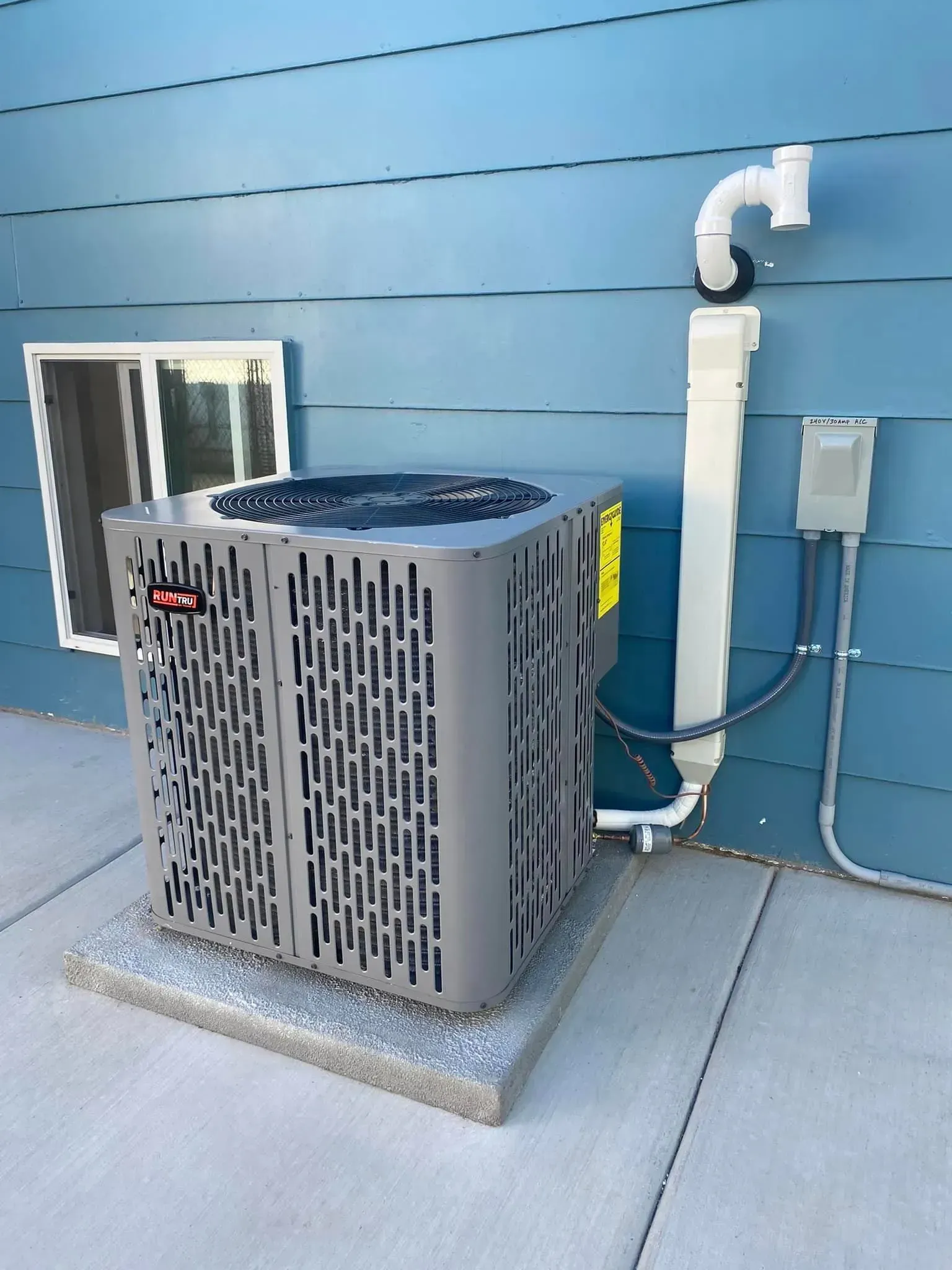 Air conditioner unit outside a blue house, next to a window and drainpipe.