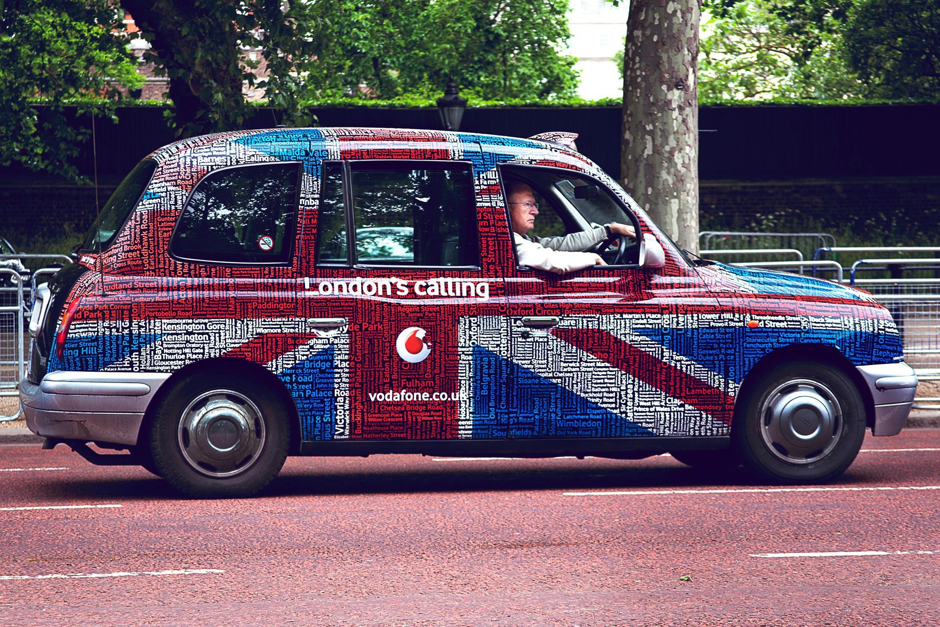 London taxi cab, painted with a Union Jack flag, driving on a city street.