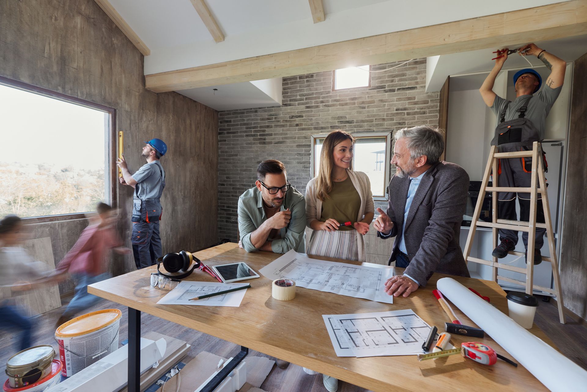 A group of people are sitting at a table in a room under construction.