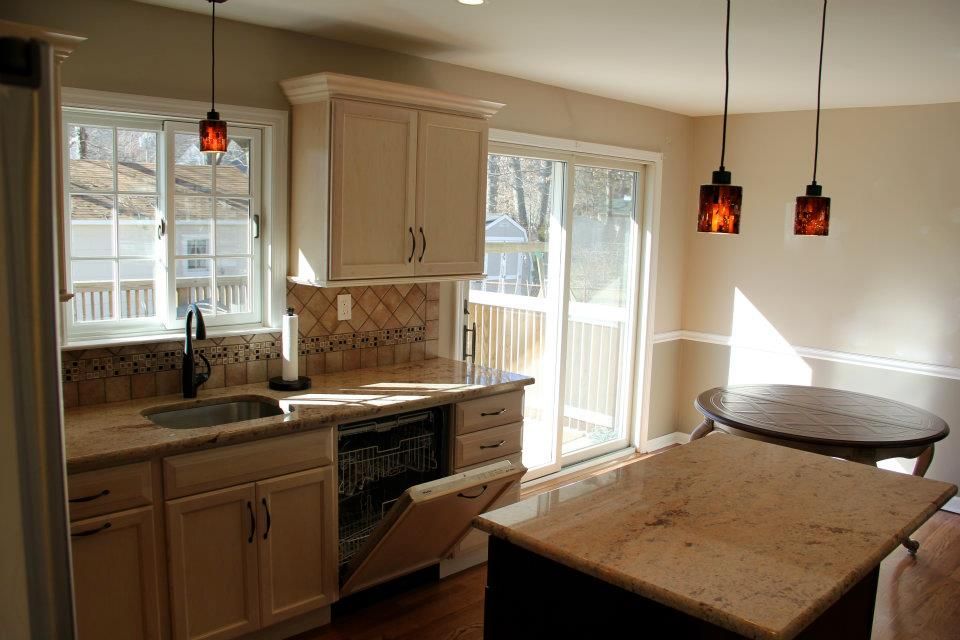Kitchen with cream cabinets, granite counters, open dishwasher, sliding glass door, and round table.