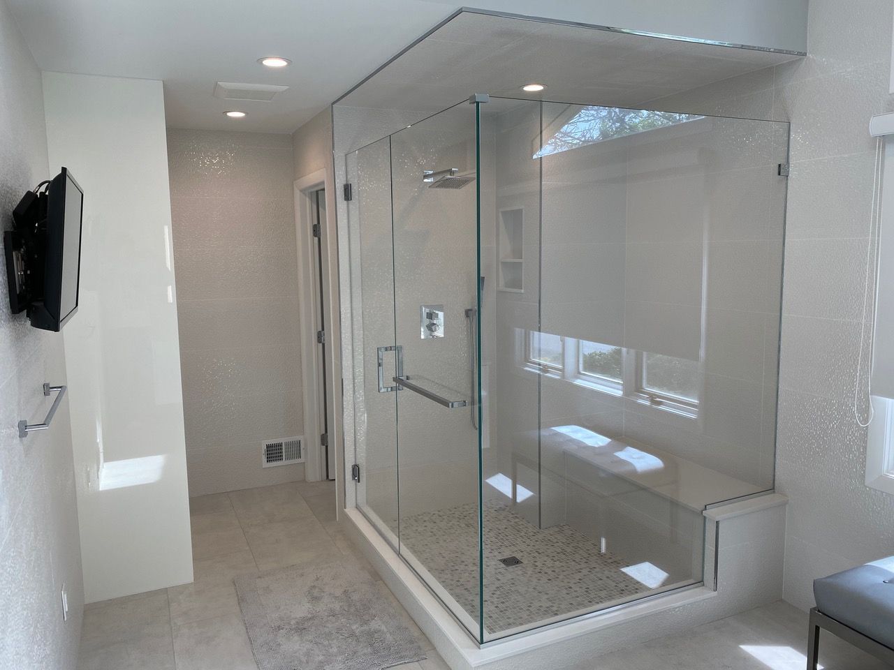 Modern bathroom with a glass shower, bench, and neutral-colored tile walls.