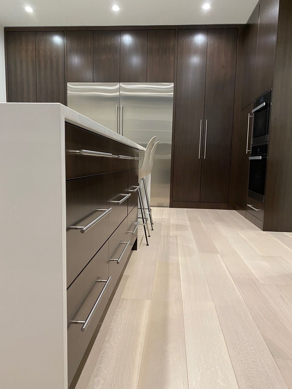 Modern kitchen with dark wood cabinets, stainless steel appliances, light wood floors, and island.