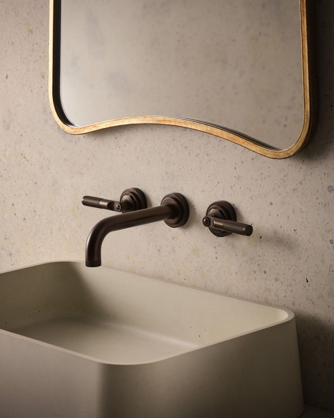 A modern bathroom sink with bronze faucet and gold-framed mirror on a concrete wall.