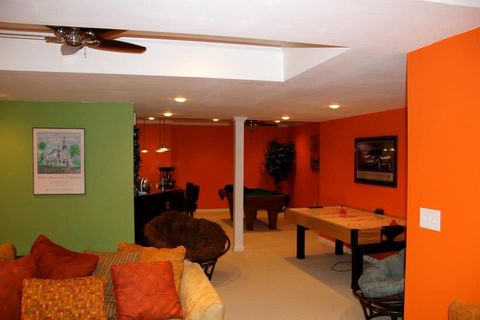 A living room with bright orange and green walls, a pool table, and a ceiling fan.
