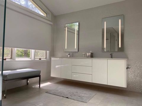 Modern bathroom with white floating vanity, mirrors, and window with shades; light gray accents.