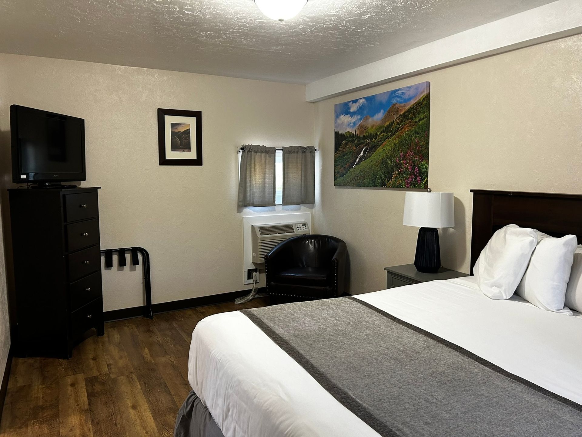 A hotel room with a king size bed , chair , television and dresser.