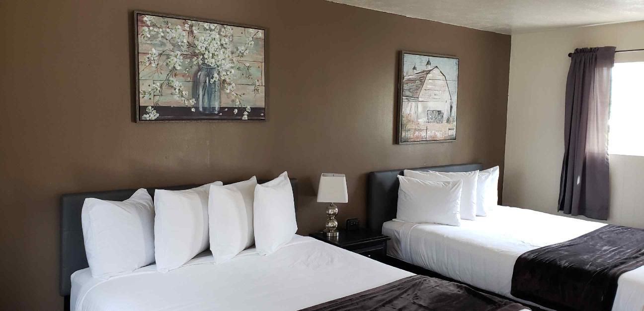 A hotel room with two beds and two paintings on the wall.