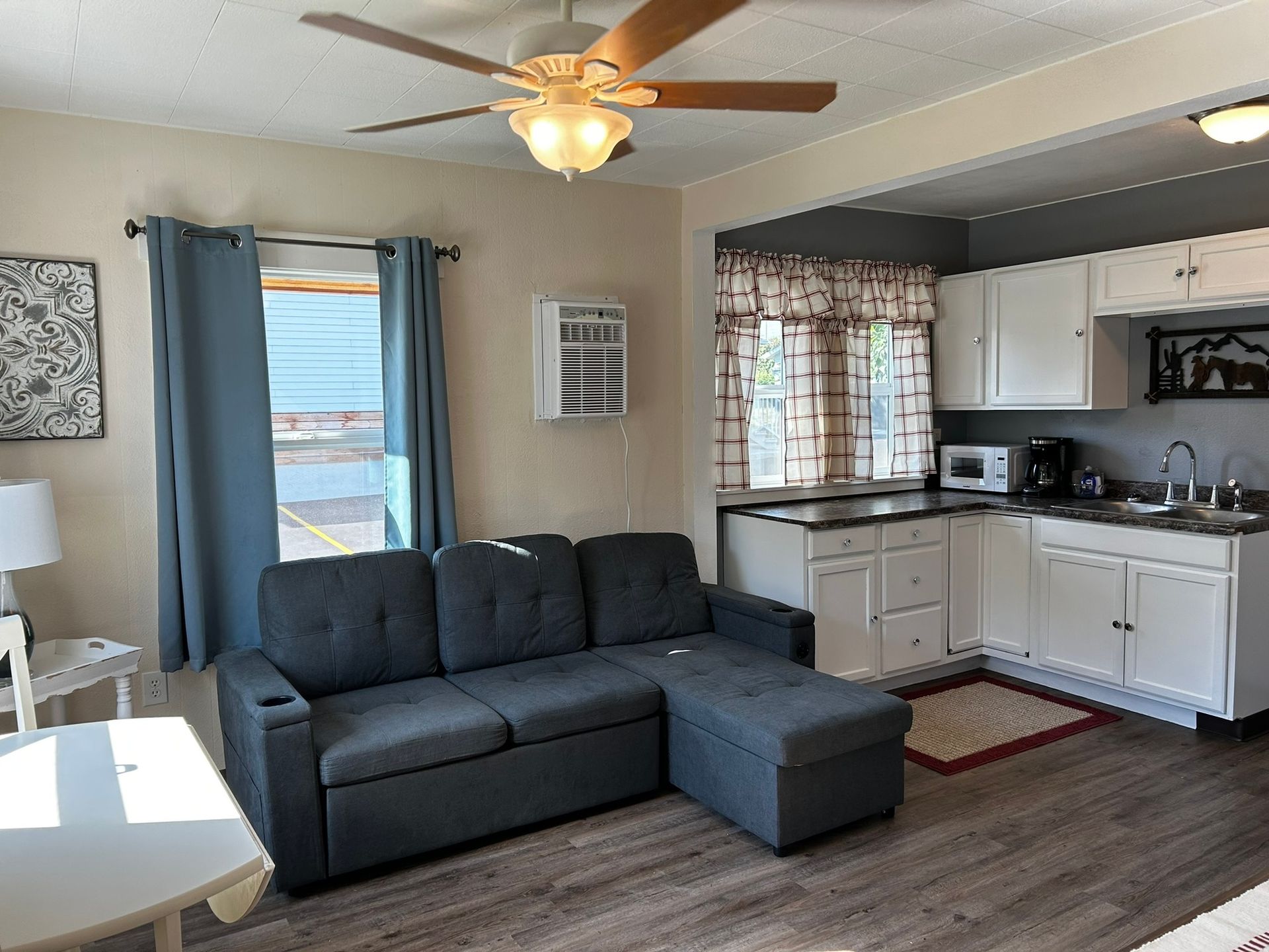 A living room with a couch and a kitchen with a ceiling fan.