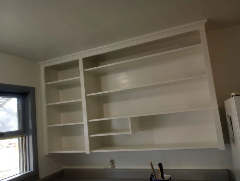 White wall-mounted kitchen cabinets with multiple open shelves, located next to a window above a countertop.