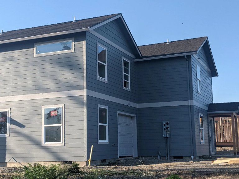A blue, two-story house under construction with a dark shingled roof, light trim, and visible electrical service equipment.