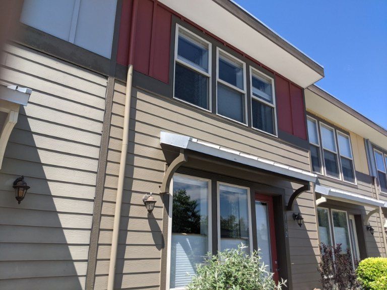 A modern two-story townhouse with beige horizontal siding, red vertical panels, and a small metal entryway awning.