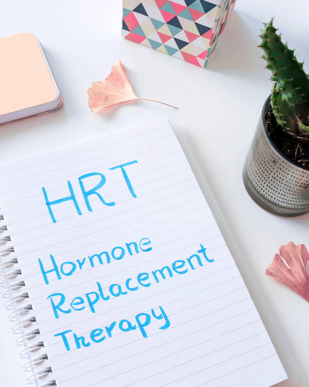 Handwritten “HRT Hormone Replacement Therapy” on a notepad with pastel desk items nearby