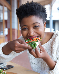 Person smiling while holding and eating a leafy salad in a bright indoor café.