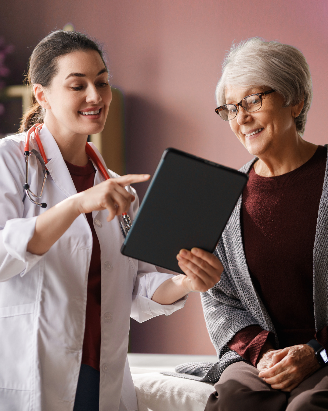 Doctor showing a tablet to an elderly patient in a clinic, both smiling.