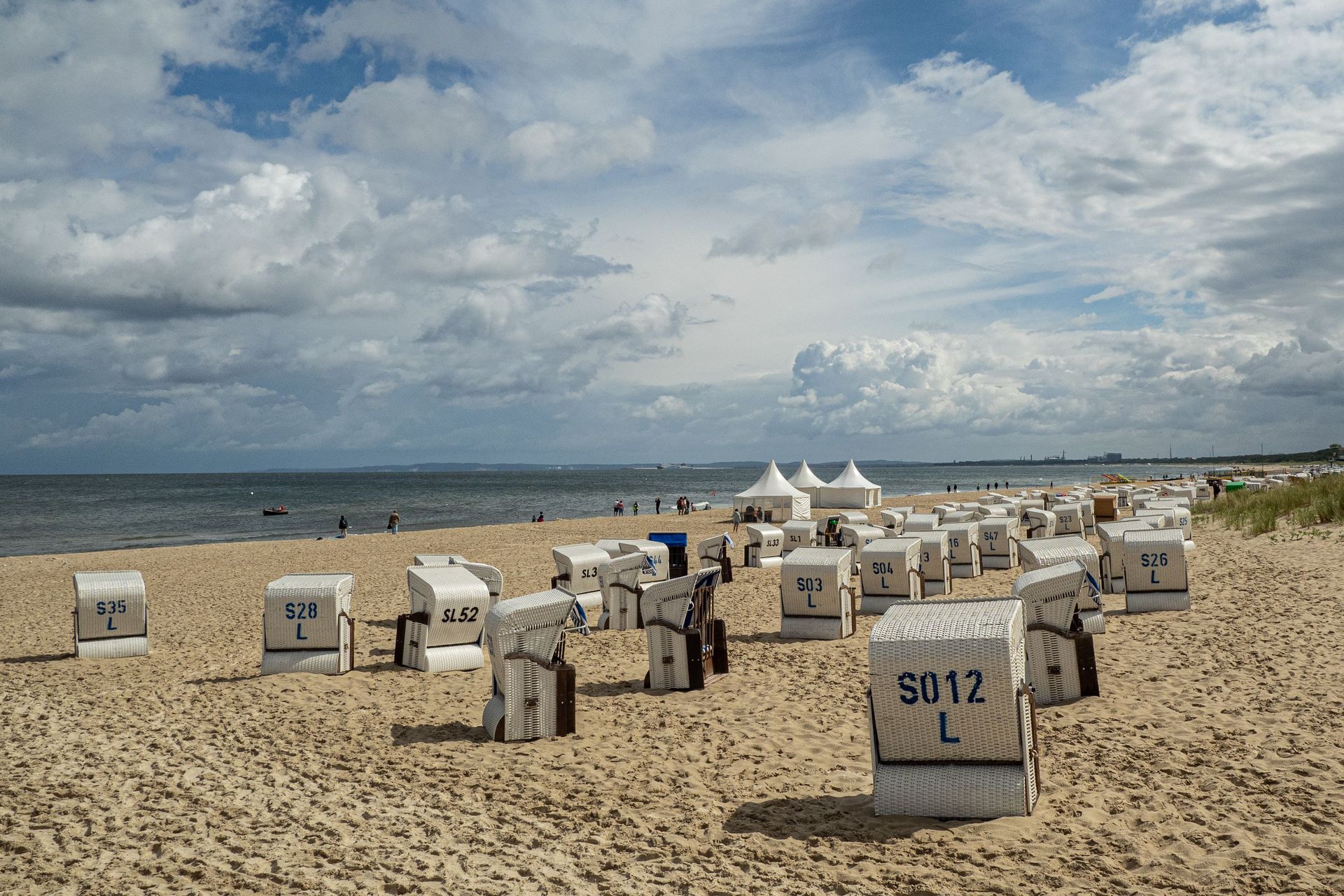 Das Bild zeigt einen Ostseestrand mit vielen weißen Strandkörben im Sand, dahinter das Meer und ein 