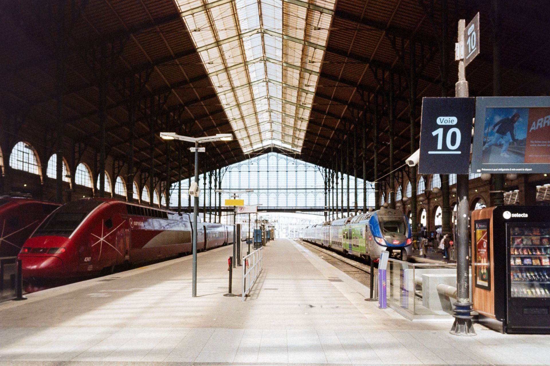 Bahnhofshalle mit mehreren Zügen an den Bahnsteigen, hoher Glasdachkonstruktion und Bahnsteig 10 in 