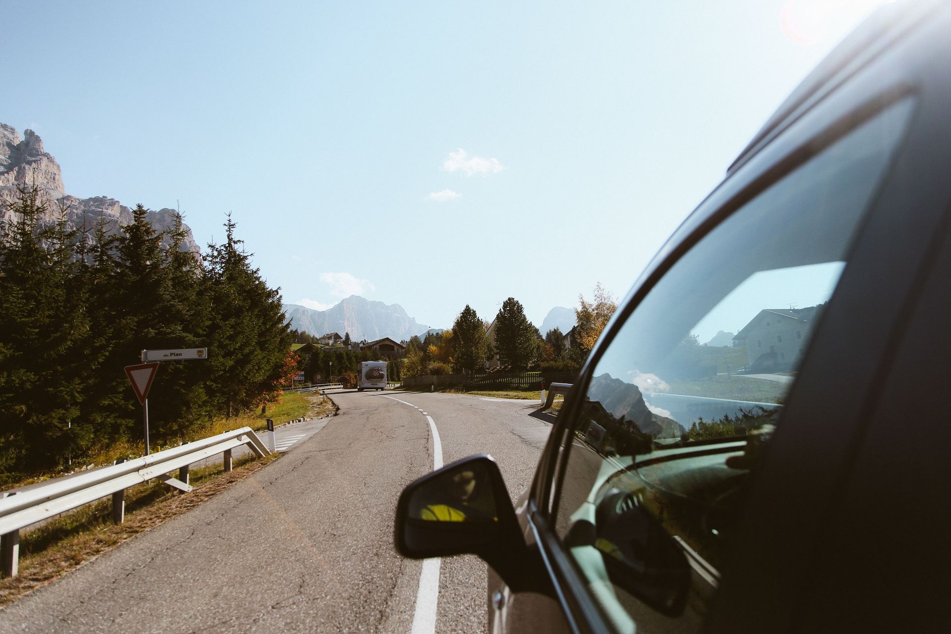 Blick aus dem Auto auf eine kurvige Landstraße mit Bergen und Wald im Hintergrund